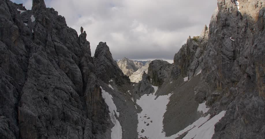Drone view of a canyon between mountain ridges with snow in the valley and the sunlight casting over the mountains in the distance