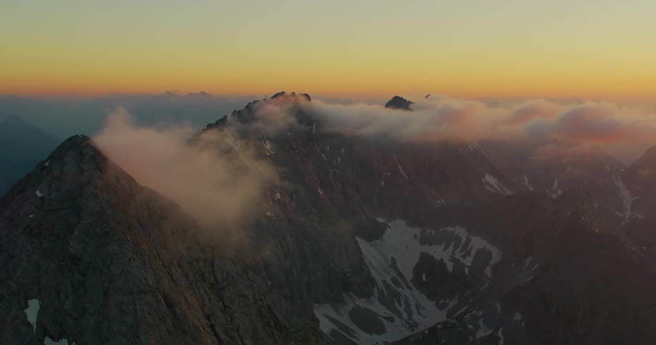 Drone view of fog covering mountain peaks as the sunlight set on the horizon casting an orange hue