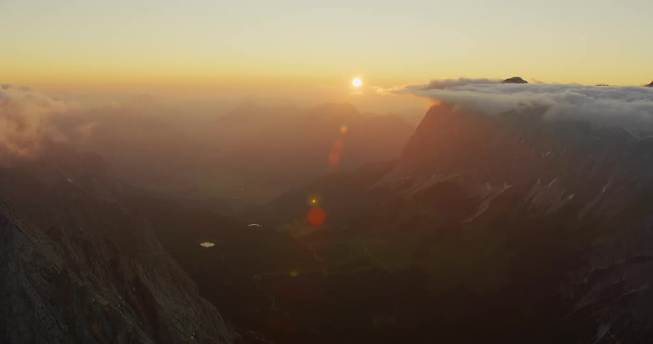Dramatic zoom of sunlight rising over the mountains with clouds on the peaks