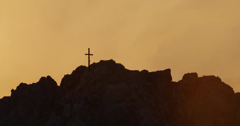 A christian cross sign on top of a rock with rough terrain during sundown