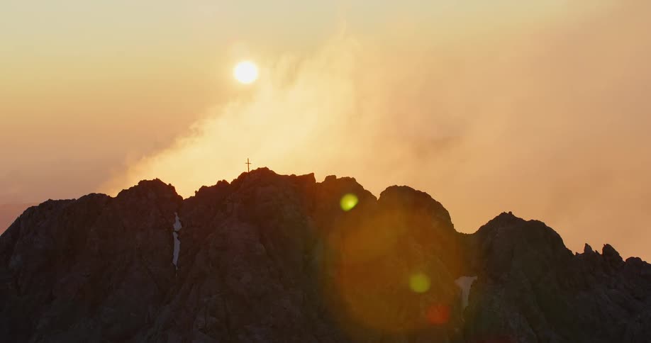 Natural landscape of a rocky mountain peak with a cross on it during dusk or dawn