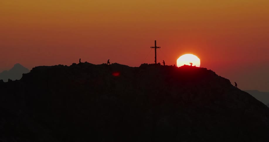 People on top of a hill with a cross and in the sky the sun is rising coloring the sky orange