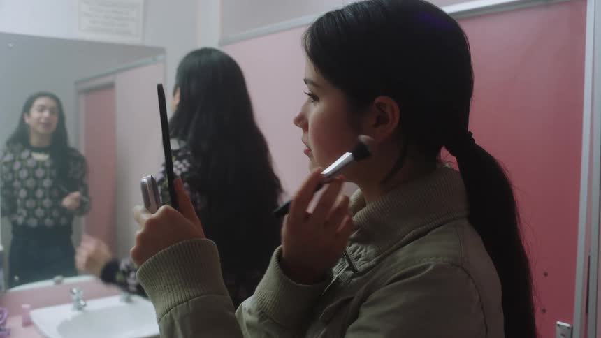 Two young women apply makeup while standing in a bathroom