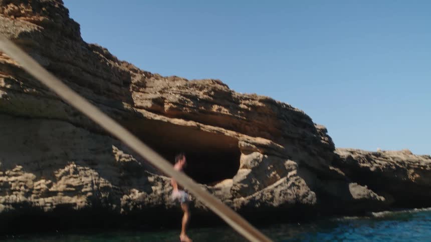 Man jumping off a cliff into water below while a boat is docked nearby