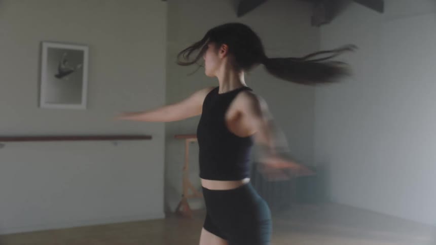 A young lady dressed in black clothing gracefully spinning around and performing yoga exercises in a hall