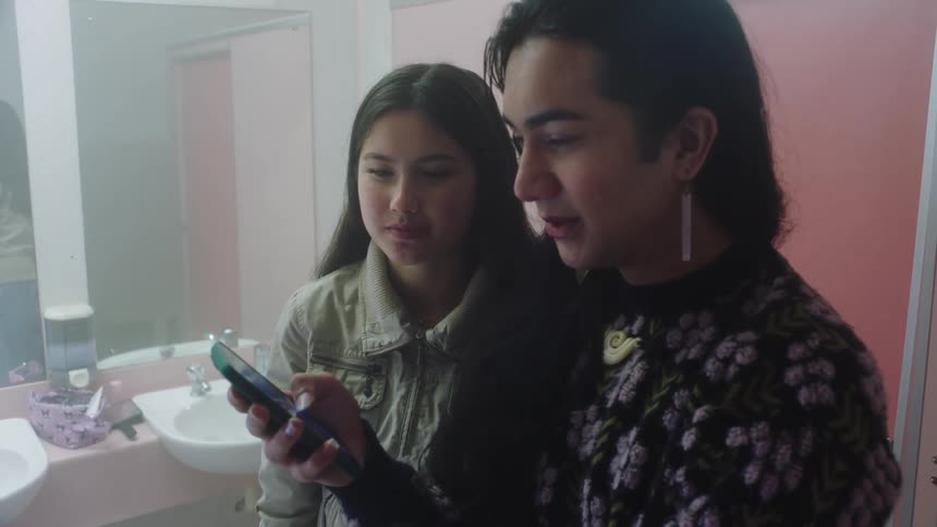 Two young people with one of them holding the cellphone and talking about something