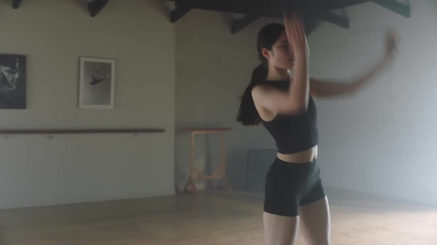 A woman wearing a black short and a top doing some dance move in an empty room with pictures on the wall