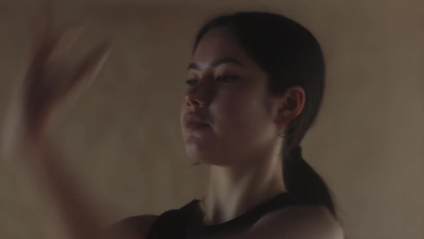 A girl raises her arms and steps backwards in a ballet dance move