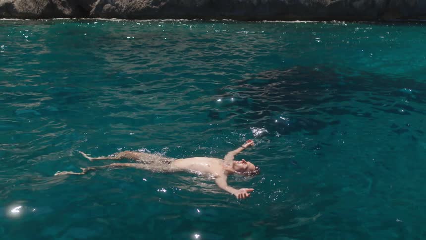 A man floating on the surface of the sparkling ocean, enjoying the sun.