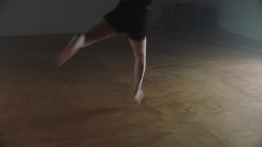 A female dancer wearing shorts points her bare toes and spins across the studio floor