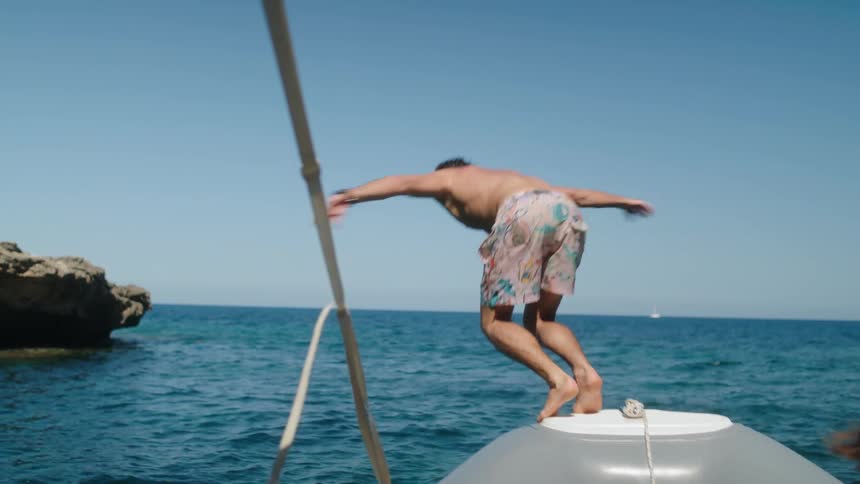 Man with swimming shorts jumps off boat into sea