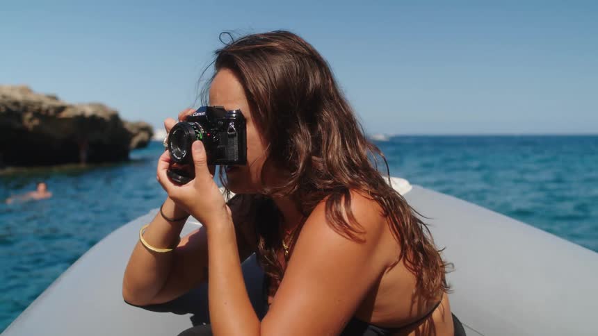 A woman in a bikini on a floating boat trying to take a photo with her camera