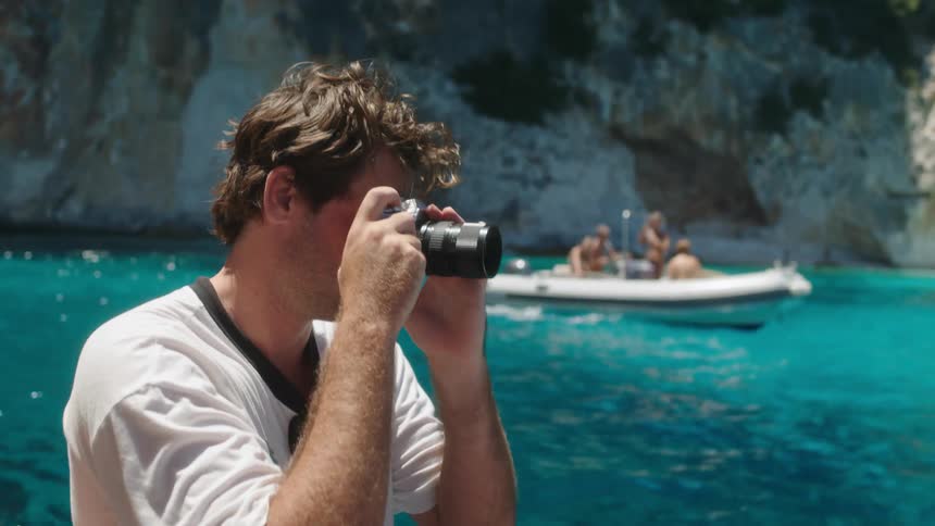 A man who is in a boat is taking pictures and behind there is another boat with women