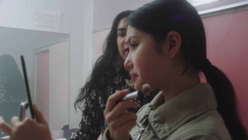 A young woman applies makeup in a school bathroom