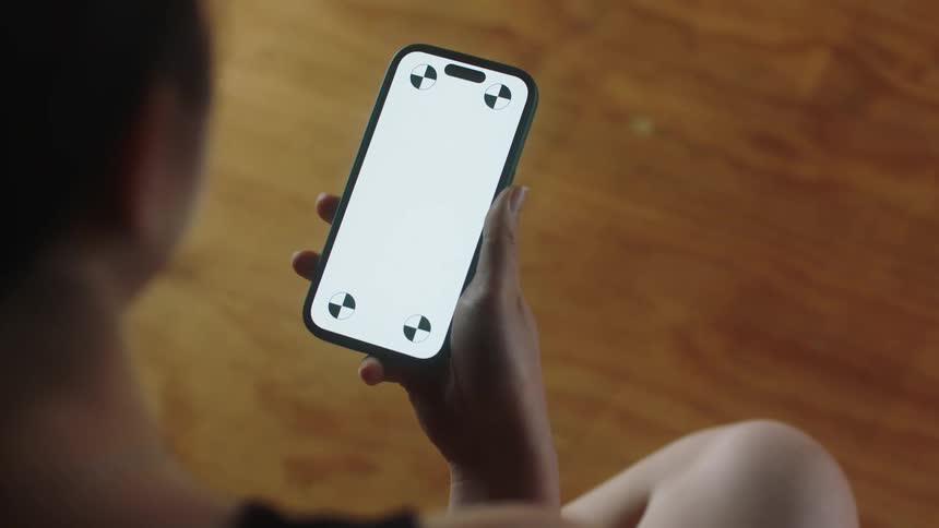 A young woman raises her smartphone up to look at its screen
