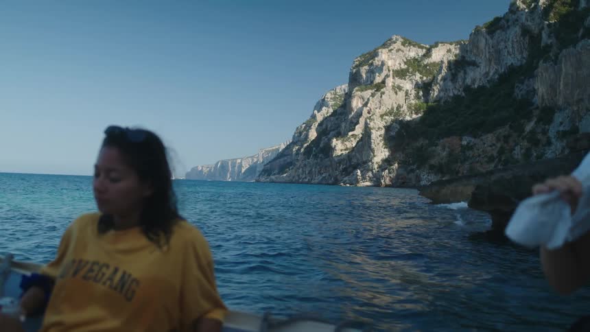 Two women seated inside a canoe on the sea with rocks visible on the left side of the water
