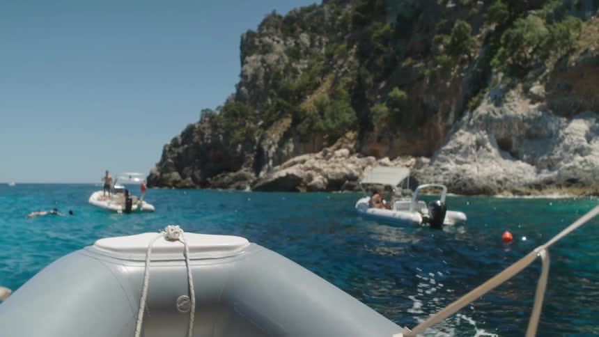 Man jumps into ocean among boats near rocky shore