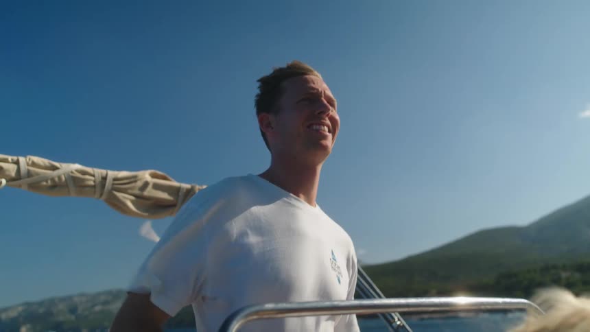 Smiling man standing up driving a boat next to the coast on a sunny day