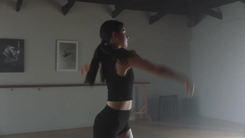 A young woman practices some dance moves alone in a dance studio