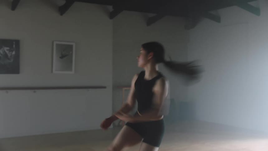 A young woman does a ballet move where she jumps with her legs in the air