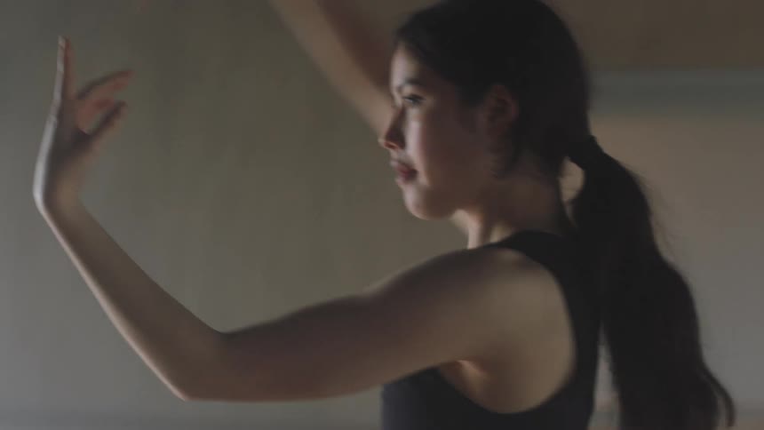 Close up of a teenage girl performing dance moves indoors as sunlight shines through windows