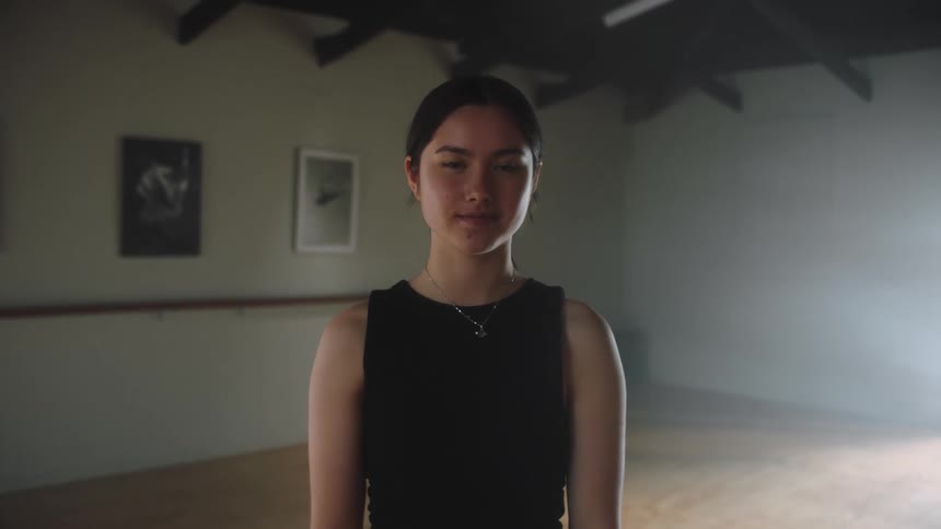 Young woman stands on a dance studio looking at the camera