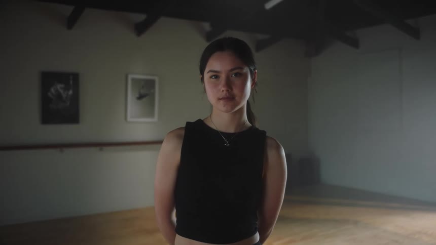 A woman standing in an empty room while wearing black top is staring at one direction