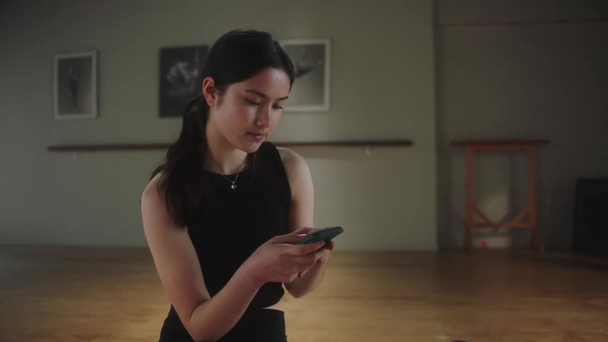 A young lady in a room looking sad glances into her phone picks up her water flask and then stands up