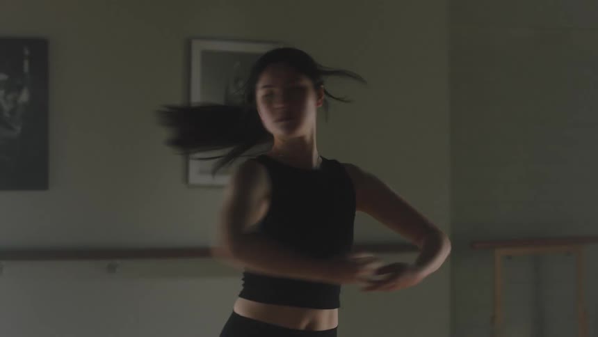 A young ballerina performs dance steps in an empty room