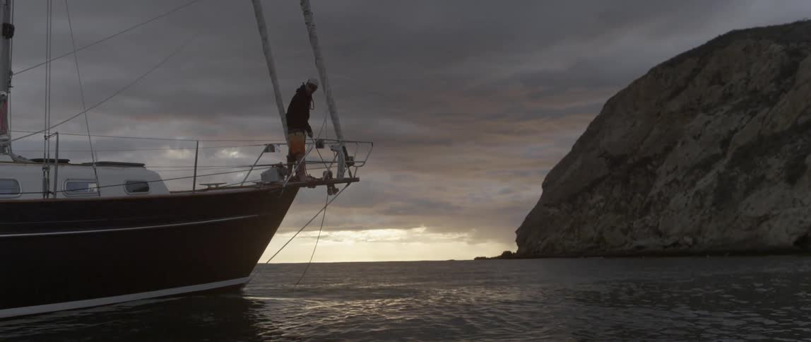 A man is standing on the front of a boat at sunset