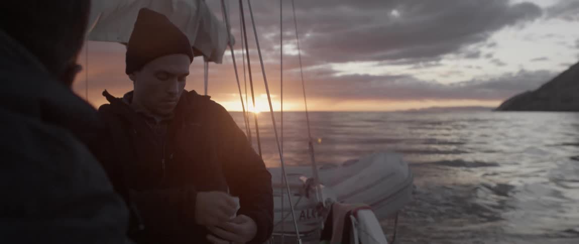 A man on a boat zips his jacket and puts his hood up at dawn