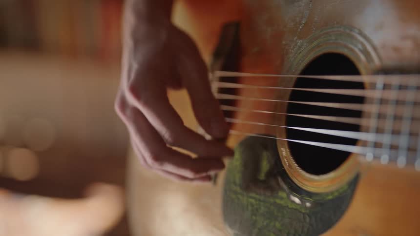 Male guitarists strums wooden acoustic guitar