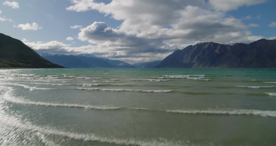 Man observing the horizon from a beach with small waves and surrounded by mountains