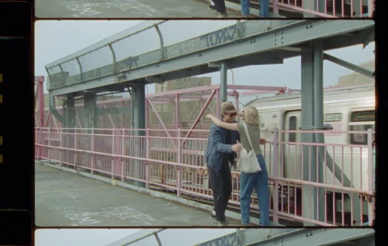 A woman runs up to a man standing at a train station and hugs him