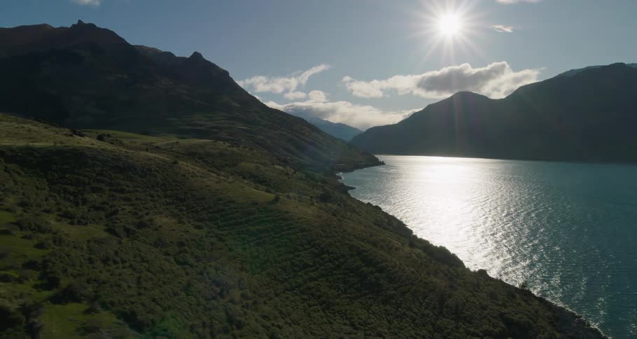 The sun shines brightly upon mountains next to a large body of water
