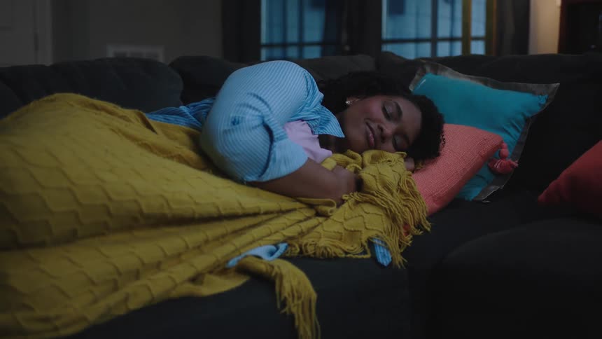 Woman sleeping on the couch gets comfortable under the blankets