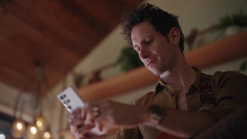 A man is typing on a cell phone and at the same time he is smiling