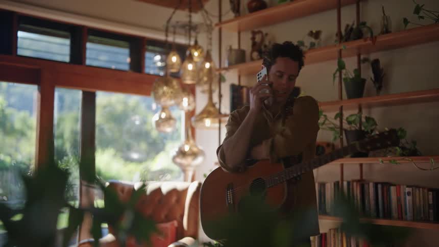 Man speaks on phone indoor with a guitar hanging on his shoulder