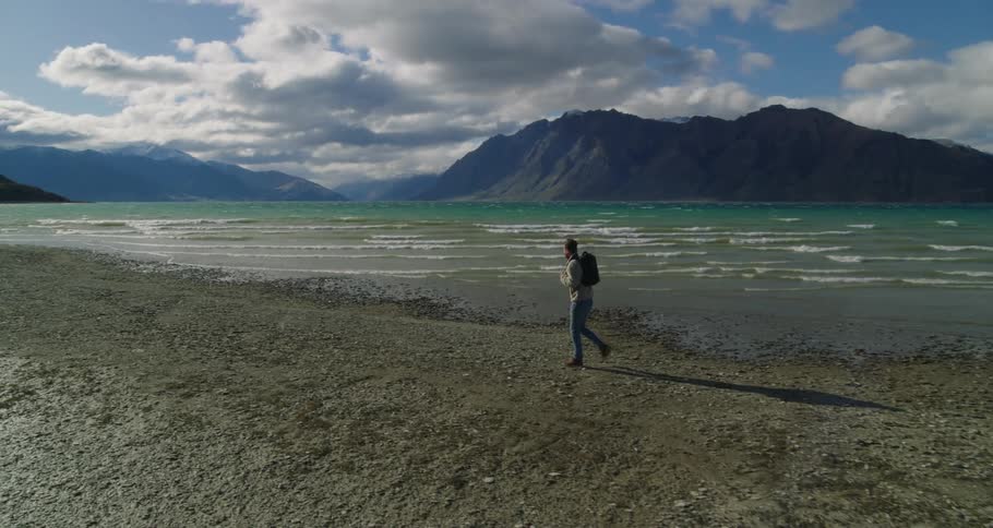 A man with a backpack walking along the sea shore and looking at the horizon