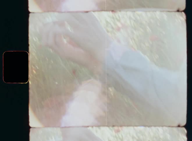 Shaky hand-held 8mm film of a young crouching man that proposes to a woman with a silver wedding ring in a red box and then he stands up and hugs his future wife amidst a field of wild red poppy flowers