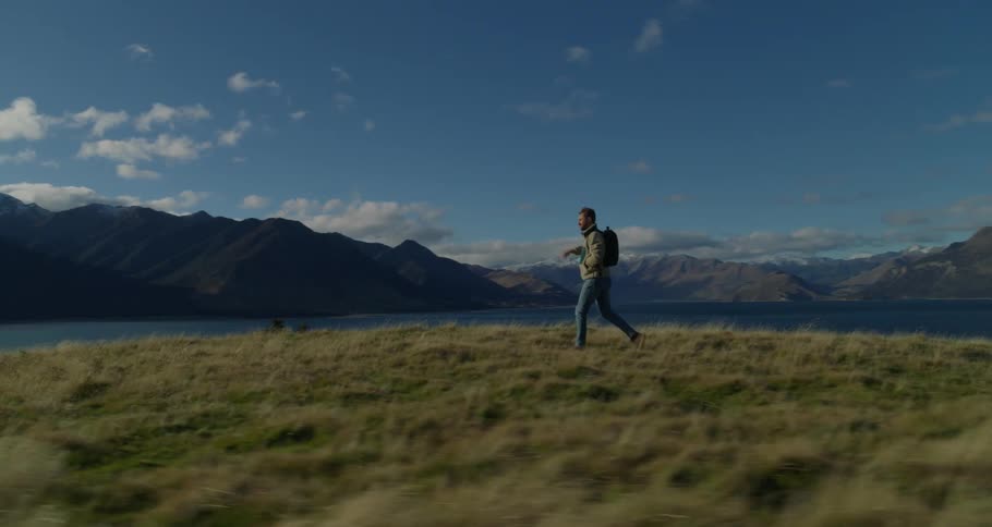 Man walking on grass field near a lake and mountains