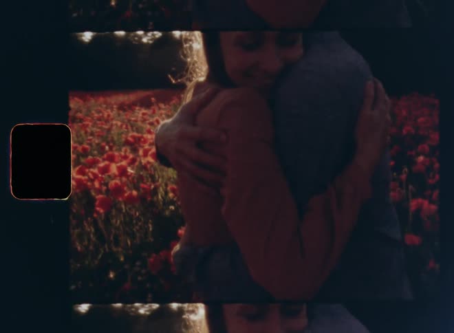 Young man and brunette woman in red dress embrace and hug while smiling happily in a flower field in nature on a sunny summer or spring day during sunset on vintage 8mm film with a nostalgic vibe and bright lens flare