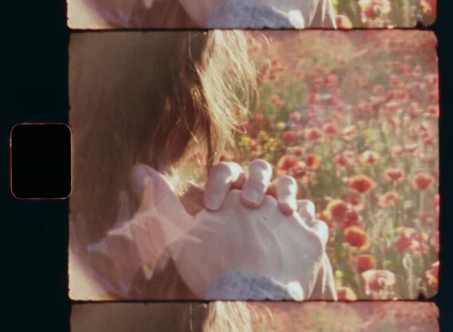 Man in grey shirt standing in field of flowers places his hand on the shoulder of brunette Caucasian woman and she takes his hand and leans her head against their joined hands in passionate way as symbol of love trust and tenderness on vintage 8mm film