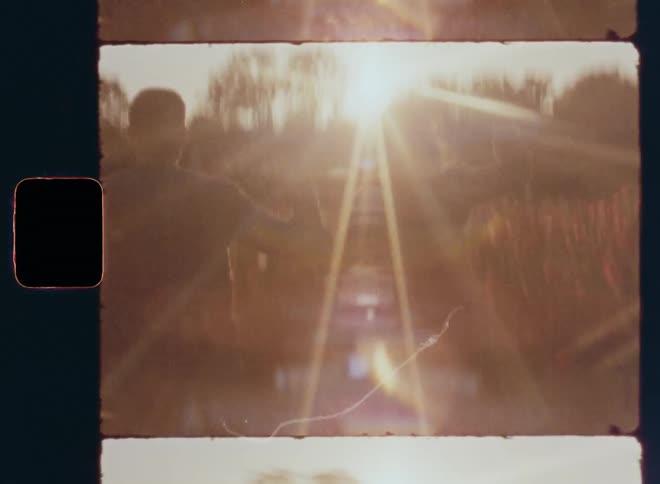 Shaky and dynamic handheld 8mm film of man and woman running as love couple in straight direction towards setting sun in weed field surrounded by colorful red flowers expressing happiness and enjoying a joyful harmonic and carefree moment
