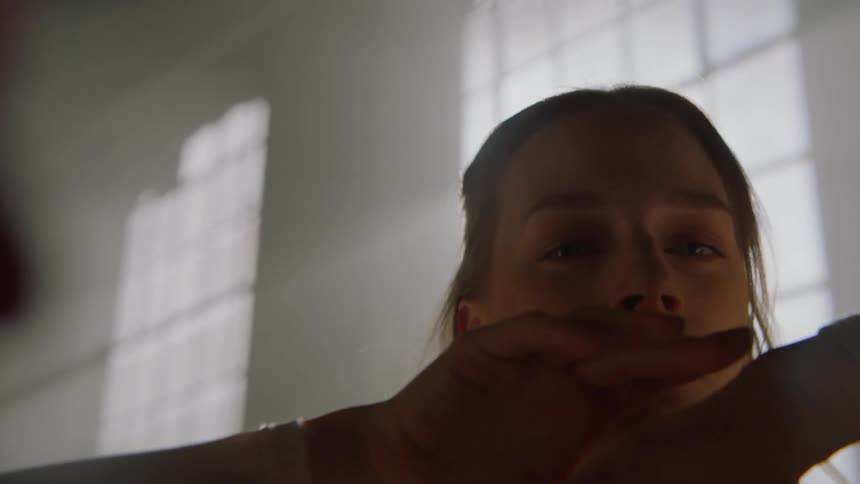 A dancer in front of a sunlit window moves her arms in hands in front of her in purposeful dance movement