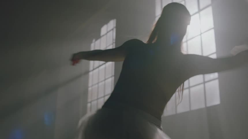 Female dancer turns and kicks out their leg in front of windows