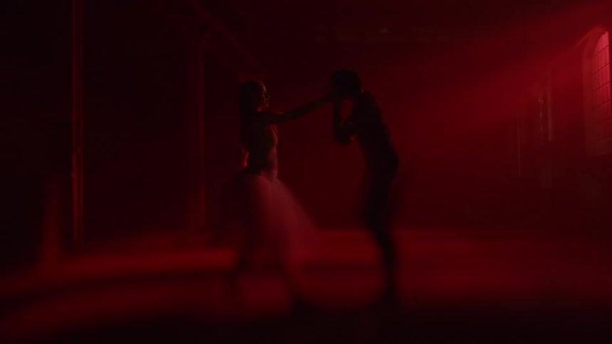 Man and woman doing ballet dance in a room under the red light