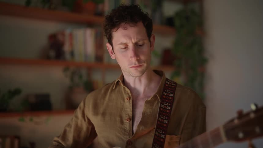 Guitarist plays guitar in room near shelves