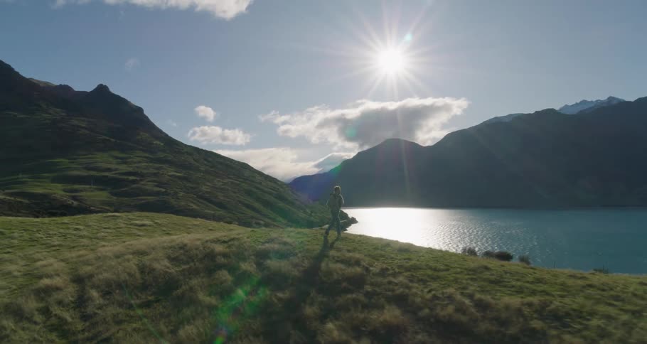 A man walking across a lawn in nature and in the background there is a huge lake and mountains