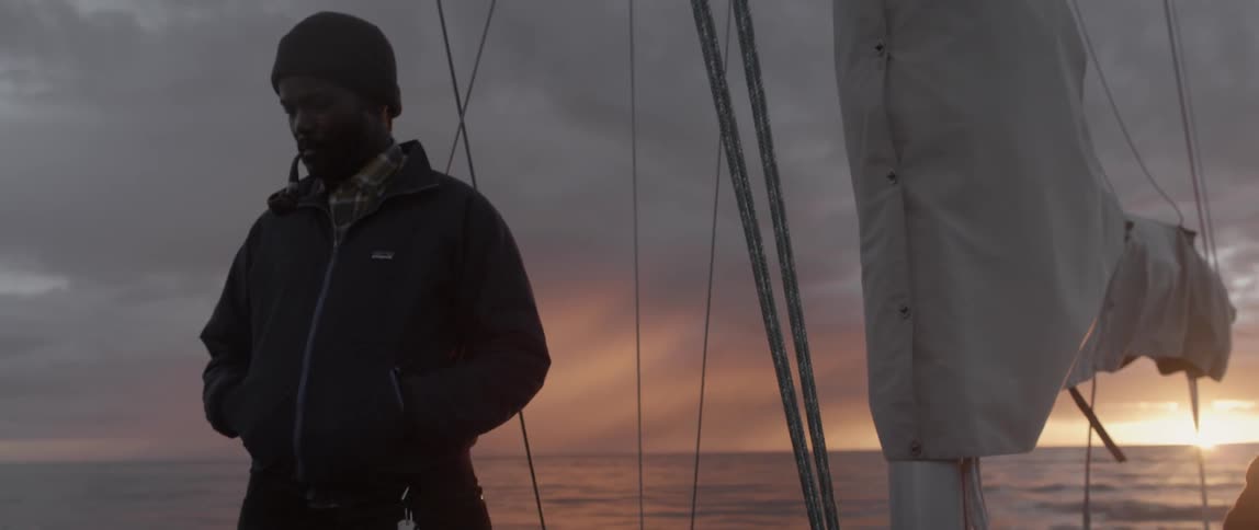A man is smoking a pipe on a boat at dawn